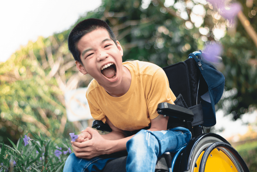 happy lad with autism in a wheelchair. He has a huge grin